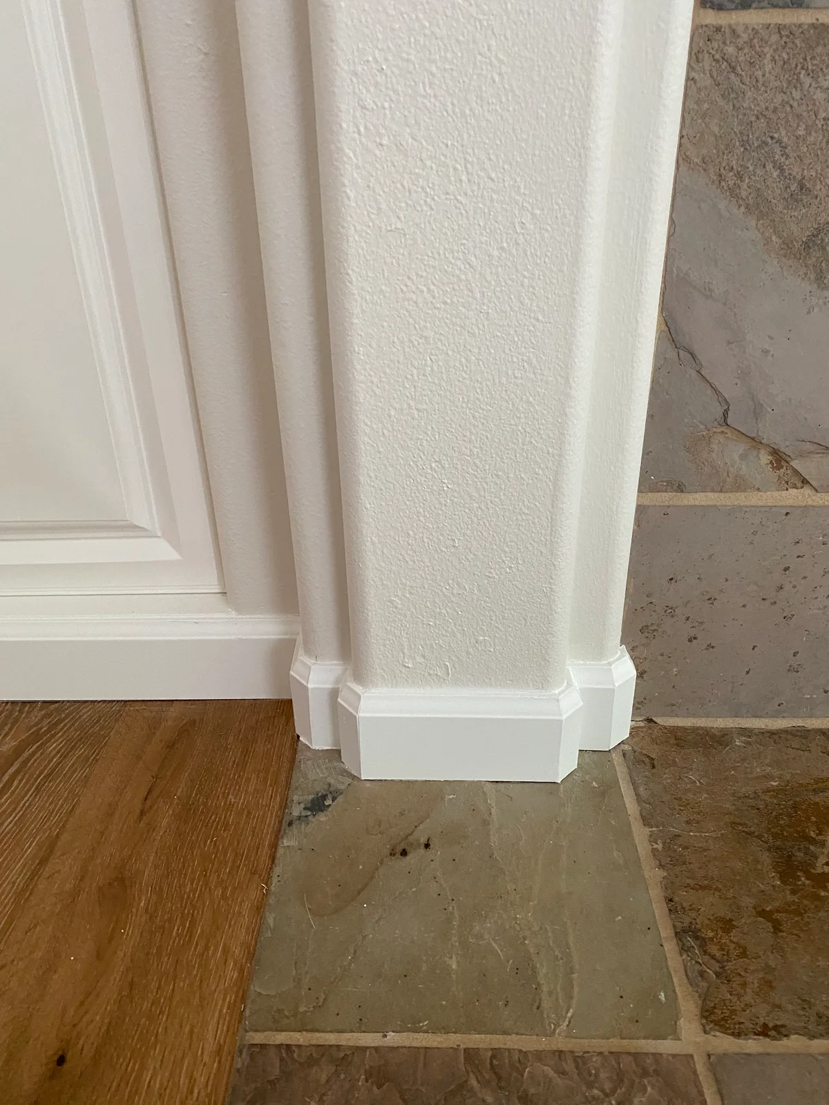White door casing and baseboard trim beside wood and stone flooring