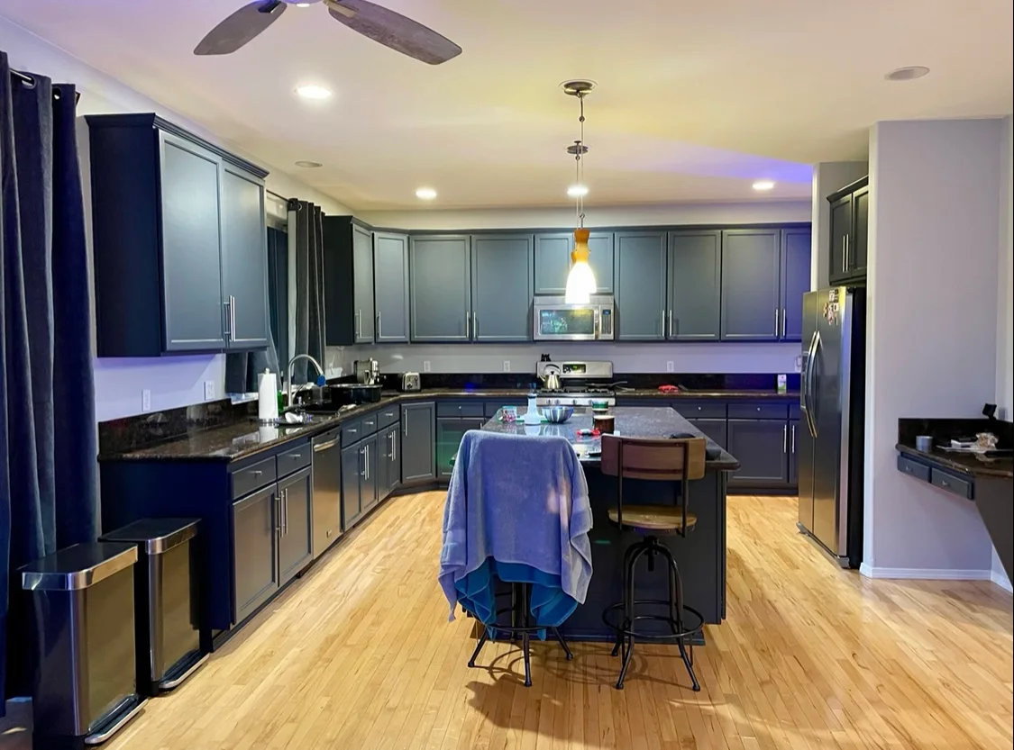 Warm wood plank flooring throughout a kitchen with blue-gray cabinets and a central island