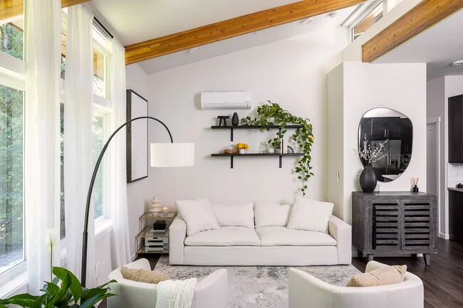 Bright living room with white walls, exposed wood beams, and a pale sofa